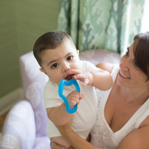 Baby in mother's lap with blue teether in mouth