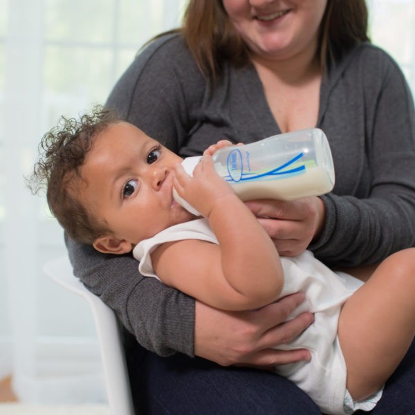 A mom holding a baby who is drinking from a Dr. Brown’s Natural Flow® Options+™ Anti-Colic Wide-Neck Bottle